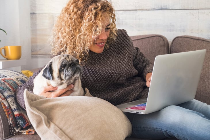 Woman on a laptop with her pug on a couch