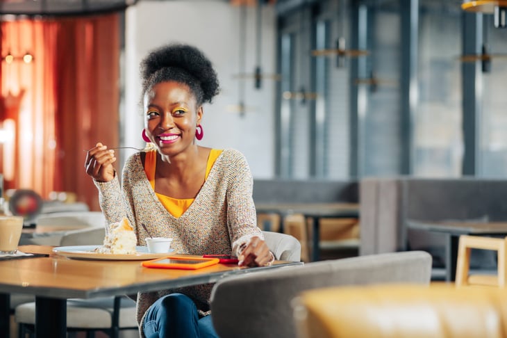 A happy woman smiles while eating a slice of pie in a restaurant