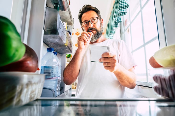 Older man looking into fridge and freezer to plan grocery list and figure out what food to eat, cook or buy