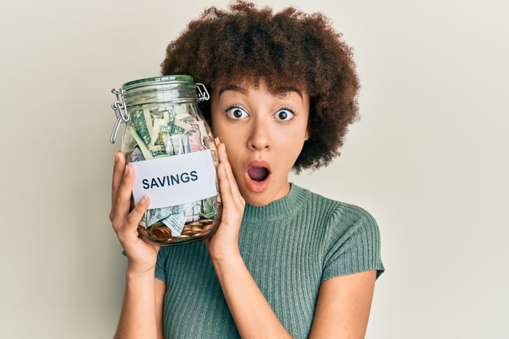 Happy woman holding a money jar stuffed with savings.